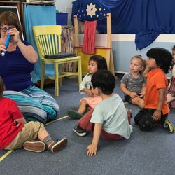 UMC Preschool - Toddlers curiously looking on as their teacher engages them in story time.