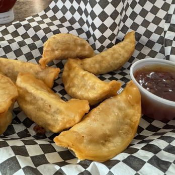 Outpost - Potstickers - Six fried potstickers served with a side of dipping sauce on checkered paper at a restaurant. - American Near Me - Anoka, Minnesota