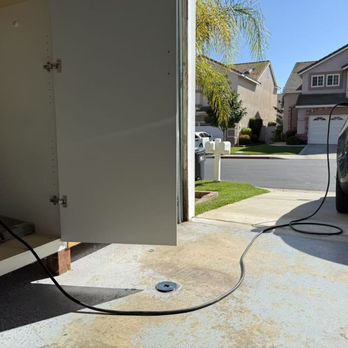 Smart Plug EV - A Tesla-certified electrician is installing an EV charger in a garage, with a view of a residential street outside, including houses and a car. - Electricians Near Me