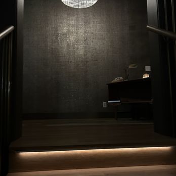 Ginger's - Upscale & lively bar - A staircase with illuminated steps ascends to a dark room featuring a textured wall, a chandelier, and a desk with a lamp and telephone. - Cocktail Bars Near Me - Dallas, Texas