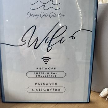 Chasing Cali Collective - WiFi - The image features a framed sign with a white background and black text, providing WiFi network details for Chasing Cali Collective. The sign includes the network name, 'Chasing Cali Collective,' and the password, 'CaliCoffee.' The design incorporates a wave illustration at the top and a WiFi icon in the center, with a simple, modern style. - Coffee & Tea Near Me - Cincinnati, Ohio
