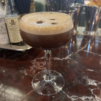 Van Atta - A dark coffee cocktail with foam and coffee beans on top is served in a coupe glass on a marble bar counter. - Bars Near Me - Telluride, Colorado