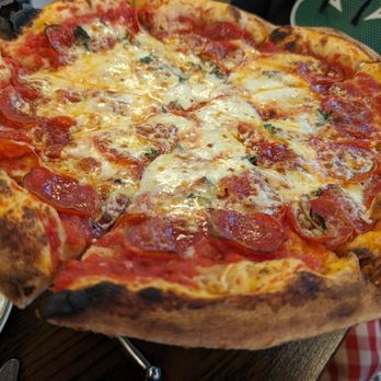 Bettola - Pepperoni. Great tasting crust, but it got thinner and thinner from the edge to the middle (100% flop and could not support ANY toppings) - A pepperoni pizza with melted cheese and tomato sauce on a wooden table, showing a slightly charred crust. - Pizza Near Me - Cranston, Rhode Island