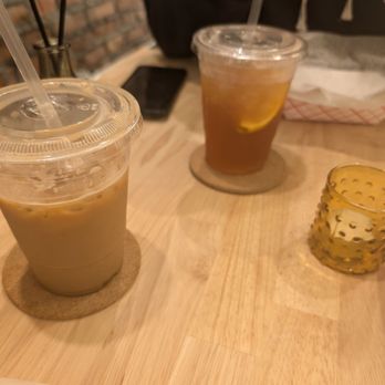 Nyla House - Iced latte with oat milk and 50/50 - Two iced beverages with straws are placed on a wooden table, each on a coaster, with a smartphone and a napkin nearby. - Cafes Near Me - Brooklyn, New York