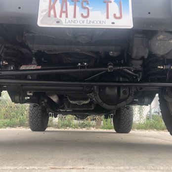 Wildside Customs - Underside of a vehicle with visible suspension parts, differential, and tires, taken in a parking lot. - Auto Customization Near Me - Naperville, Illinois
