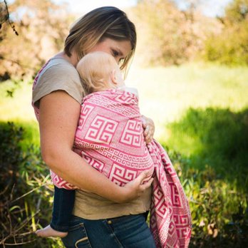 Mama Goose Postpartum - White woman holding a blonde child in a pink sling, background is a green forested area. - Childbirth Education Near Me Mama Goose Postpartum - White woman holding a blonde child in a pink sling, background is a green forested area. - Childbirth Education Near Me