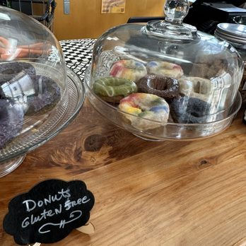 Tru Cafe - Colorful donuts are displayed in a glass case on a wooden counter at a cafe, with a small chalkboard sign indicating they are gluten-free. - Vegan Near Me - Hammond, Louisiana