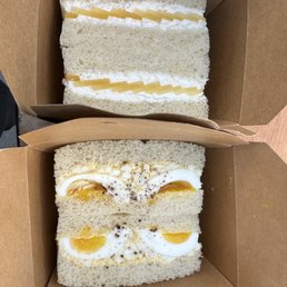 Egg Salad Sando - Two sandwiches with egg salad, soft white bread, and minimal fillings are placed in brown takeout boxes, ready for serving.