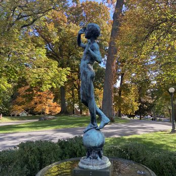 Lyndhurst - A bronze sculpture of a woman standing on a globe, positioned in a park with trees displaying fall foliage and a fountain base. - Museums Near Me - Tarrytown, New York