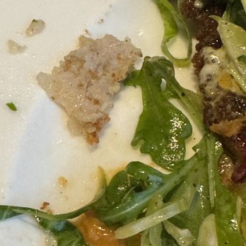 Fanny's - Undercooked, almost raw, paper thin pork chop. Disgusting. - The image shows a close-up of a plate with a small, partially eaten piece of food, possibly a breaded or baked item, alongside fresh green salad leaves. The plate appears to have remnants of sauce or dressing, indicating a recent meal. The setting suggests a restaurant environment, with focus on the food presentation and ingredients. - Wine Bars Near Me - Bloomfield, New Jersey