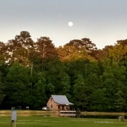 The full moon hangs low over the lake cabin, as the last rays of the sunset grace the tops of the trees.