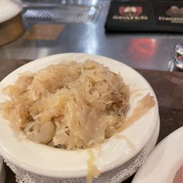 Healthy side of fresh sauerkraut! - A bowl of cooked sauerkraut is placed on a white plate with a decorative paper doily, in a restaurant setting at Chef Klaus' Bier Stube in Frankfort, IL.