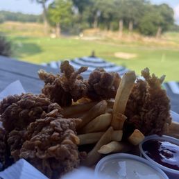 Chicken and fries but up close - A plate of fried chicken and French fries with dipping sauces is set on a wooden table outdoors, overlooking a golf course.