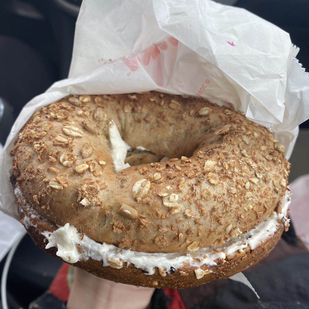 Dunkin' - a person holding a bagel covered in frosting - Donuts Near Me - Surf City, North Carolina Dunkin' - a person holding a bagel covered in frosting - Donuts Near Me - Surf City, North Carolina
