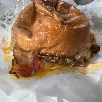 Union Kitchen - A burger with a toasted bun, bacon, melted cheese, and sauce is placed on parchment paper, with some sauce dripping. - Coffee & Tea Near Me - Washington, DC, District of Columbia