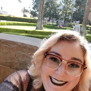 Atomic Babes - Started out Blonde, first time dying my hair - A woman with blonde, wavy hair and glasses is smiling in a selfie outdoors, with a garden and statues in the background. - Hair Salons Near Me - Sonora, California