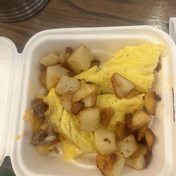 First Watch - My LEFTOVERS - A white takeout container contains scrambled eggs, diced potatoes, and small pieces of cooked sausage, placed on a wooden table. - Breakfast & Brunch Near Me - Stuart, Florida