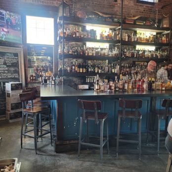 Local Feed - An indoor bar with a brick wall, shelves filled with liquor bottles, and a counter with bar stools, in a restaurant setting. - Southern Near Me - Georgetown, Kentucky