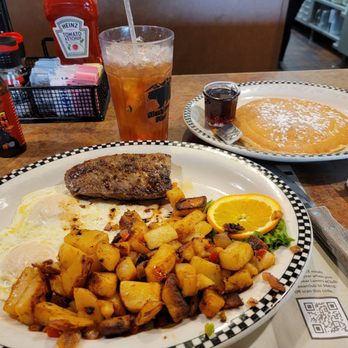 Black Bear Diner Gilbert - Steak and egg special - A breakfast meal featuring eggs, roasted potatoes, sausage, and orange slices on a checkered plate at Black Bear Diner, with a side of pancake and syrup. - American Near Me - Gilbert, Arizona