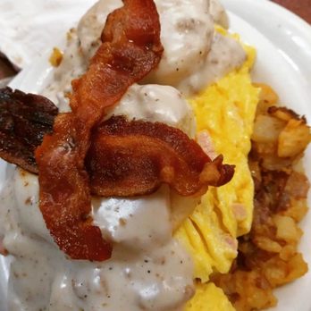 The Shack - The kitchen sink - A close-up image of a breakfast dish showing scrambled eggs, crispy bacon strips, and a portion of creamy gravy with black pepper. The eggs are yellow and fluffy, while the bacon appears well-cooked with a reddish-brown color. The gravy is thick and white, covering some of the eggs and bacon. The food is served on a white plate, with some additional food items visible on the side. - Breakfast & Brunch Near Me - Waterford, Connecticut