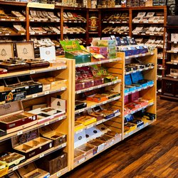 Spacious cigar shop interior featuring organized displays of premium handcrafted cigars, humidors, and popular cigar brands...