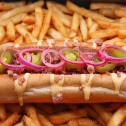 B'Shake Burger - Juicy beef hot dog on a soft bun with bacon crumble, pickled onions, jalapeños, B'Shake hot sauce & cheddar sauce, served with crispy fries.