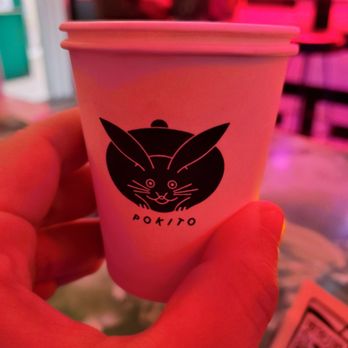 Pokito - A person holds a white paper cup with a black rabbit logo and the word 'Pokito' in a vibrant, neon-lit environment, likely inside a bar or cafe. - Cocktail Bars Near Me - Brooklyn, New York