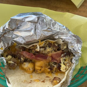 Moke's Coffee & Kitchen - Fantastic Four taco - A breakfast taco filled with scrambled eggs, bacon, sausage, and melted cheese, served in a foil wrapper on a green basket. - Coffee & Tea Near Me - Eugene, Oregon