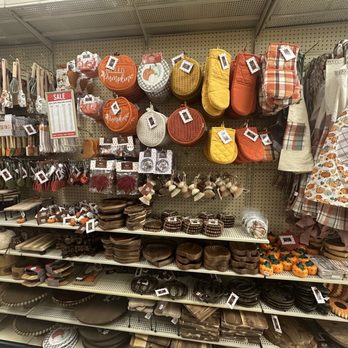 At Home - The image shows store shelves stocked with fall-themed kitchen and home decor items. The top shelf features oven mitts and pot holders in pumpkin and autumn colors, with some labeled 'Hello Pumpkin.' Below, there are decorative pumpkins, bowls, and other kitchen accessories in earthy tones. To the right, there are fabric aprons and dish towels with fall patterns. The shelves are organized with various items related to seasonal home decor and kitchen accessories. - Home Decor Near Me - Abingdon, Maryland