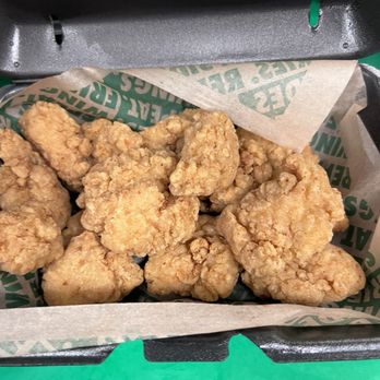 Wingstop - a box of fried chicken - Several pieces of fried chicken are arranged in a takeout container with branded paper lining, likely from a fast-food restaurant. - Chicken Wings Near Me - Niles, Illinois