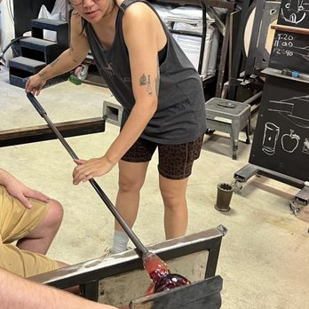 Ghost Pepper Glass - Holding the board to flatten the base while the instructor rolls the piece. - Glass Blowing Near Me - Austin, Texas Ghost Pepper Glass - Holding the board to flatten the base while the instructor rolls the piece. - Glass Blowing Near Me - Austin, Texas