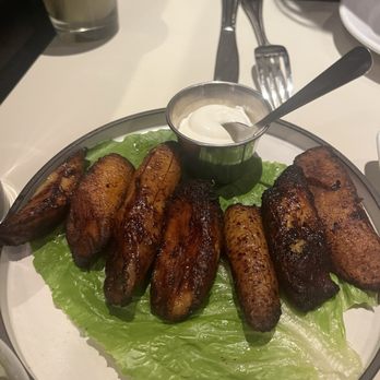 Cafe con Leche - A plate of grilled chicken wings served on a bed of lettuce with a small cup of dipping sauce, set on a restaurant table with utensils. - Mexican Near Me - Chicago, Illinois