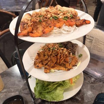 Dan Da - FOUR SEASON TOWER - A three-tiered serving tray holds Vietnamese cuisine, featuring grilled meats, noodles, and fresh vegetables, served on white plates. - Vietnamese Near Me - Aurora, Colorado