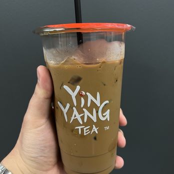Yin Yang Tea - Vietnamese coffee - A person holds a large plastic cup of iced Vietnamese coffee from Yin Yang Tea, with a black straw and a red plastic lid, against a plain gray background. - Bubble Tea Near Me - Pasadena, California