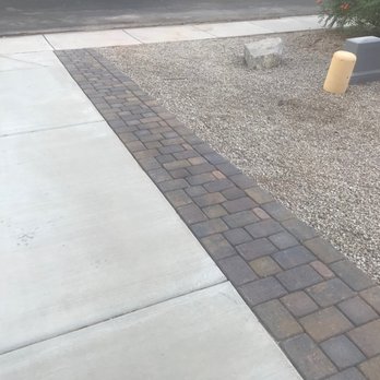 Legacy Green Solutions - Extended the driveway to  keep people from ending up in the grass when they exit the car. - Concrete sidewalk with a brick border runs alongside a gravel area containing protective barriers and a bush. - Landscaping Near Me - Mesa, Arizona