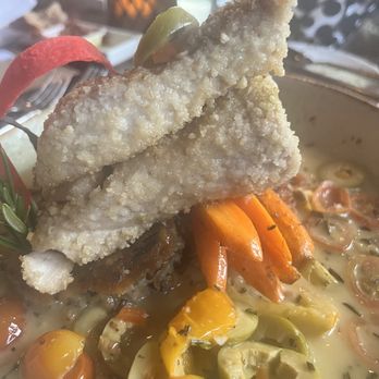 Desert Bistro - Fish special - Two fried fish fillets are stacked on top of a vegetable medley with cherry tomatoes, carrots, and olives in a creamy sauce. - New American Near Me - Moab, Utah