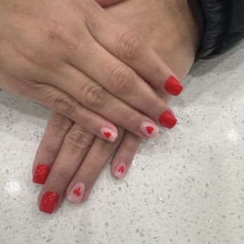 Java Nail & Spa - UV Gel set and Gel Polish - Close-up of two hands with manicured nails, featuring red polish and heart designs, resting on a speckled table surface. - Nail Salons Near Me - North Haven, Connecticut