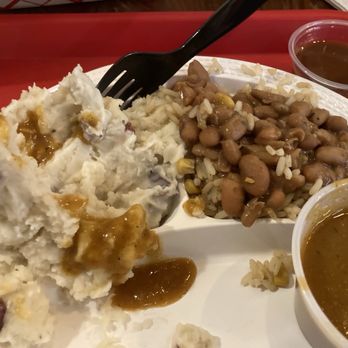 Willards Real Pit BBQ - A divided white plate holds a serving of mashed potatoes topped with gravy, alongside baked beans mixed with rice and corn. Two small cups of gravy are placed on the tray, which is red in color. The food appears to be part of a casual dining setting, with the focus on the food presentation. - Barbeque Near Me - Reston, Virginia