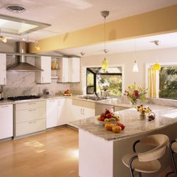 3 Sons Home Solutions - A bright, open-concept kitchen features light-colored cabinetry, granite countertops, an island with bar stools, and track li...