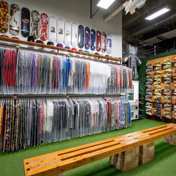 Private Selection - A retail store displays skateboards on the wall above clothing racks and shoes on wooden shelves, with artificial grass flooring. - Men's Clothing Near Me - Dallas, Texas