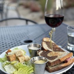 The Cheese Board South Reno - Hot pastrami and cesar salad with as glass of pinot noir