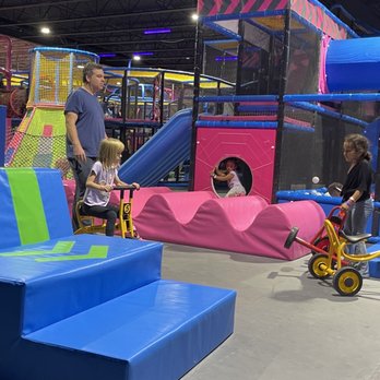 Flying Squirrel - Trikes in the adventure park - Children are riding tricycles and playing on a slide inside an indoor play area with colorful equipment. - Trampoline Parks Near Me - Ottawa, Ontario