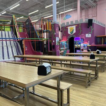 Kids Empire Paramus - A spacious indoor play area features multiple slides, climbing structures, and arcade games, with wooden tables and benches in the foreground. - Kids Activities Near Me - Paramus, New Jersey