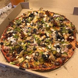 A pizza with toppings including green peppers, black olives, onions, and sausage, served in an open box on a countertop.