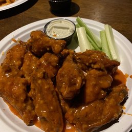 Hot garlic - Buffalo chicken wings served with celery sticks and two dipping sauces on a white plate.