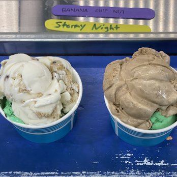 Aldo's Bakery - Cookie Dough mixed with Mint Oreo and 'Coffee & Donuts' mixed with Mint Oreo. - Two cups of ice cream with different flavors are placed on a blue surface, with colorful labels above indicating flavors. - Bakeries Near Me - New Shoreham, Rhode Island