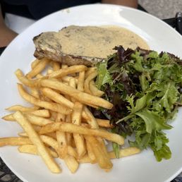 Steak Au Poivre - A white plate holds French fries, a salad with mixed greens, and a steak topped with a creamy sauce, served outdoors.