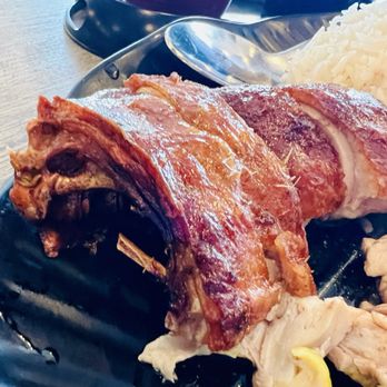 IT DIMSUM - A roasted meat with crispy skin and tender interior is presented on a black plate, accompanied by white rice and some sliced meat. - Dim Sum Near Me - Albuquerque, New Mexico