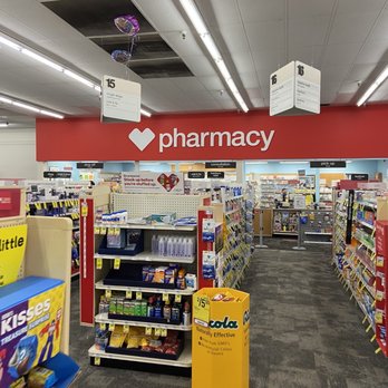 CVS Pharmacy - The image shows the interior of a CVS Pharmacy store, featuring aisles filled with various products such as medications, health supplies, and personal care items. Overhead signs indicate different sections, including cough drops, cold & flu, and consultation areas. The store has bright lighting, a red pharmacy sign with a white heart logo, and a ceiling with fluorescent lights and some missing ceiling tiles. Balloons are attached to the ceiling, and the floor is carpeted. - Drugstores Near Me - Riverside, California