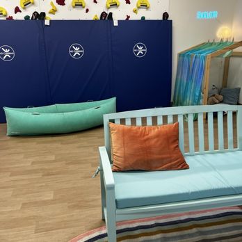 Holistic Home Designs - Colorful bench, rug, rock climbing wall, sensory hug canoe, quiet nook in the background. - Interior Design Near Me Holistic Home Designs - Colorful bench, rug, rock climbing wall, sensory hug canoe, quiet nook in the background. - Interior Design Near Me
